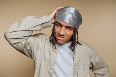 Kafası karışmış genç bir adam Durag ve günlük gömlek giyiyor.