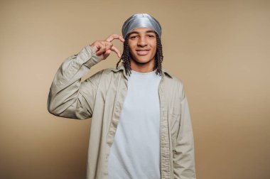 Durag giyen genç bir adam bej arka planda el hareketi yapıyor..