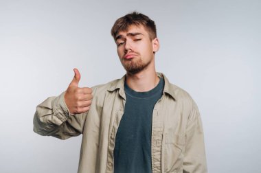 Sakallı genç bir adam neşeli bir ifadeyle baş parmağını kaldırıyor..