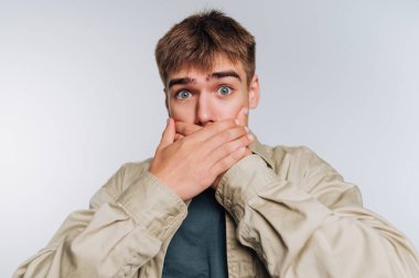 Ağzı ellerle kaplayan genç adam, şaşırmış ifade..