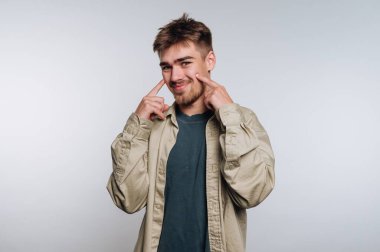 Genç adam gülümsüyor ve arka planda yanaklarını gösteriyor..