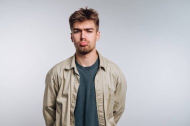 Suratı asık genç bir adam, arka planda sıradan kıyafetler giyiyor..