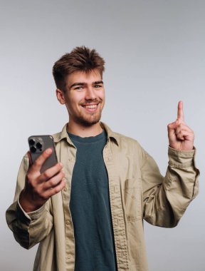 Genç adam akıllı bir telefon tutuyor ve yukarı bakıyor, gülümsüyor..