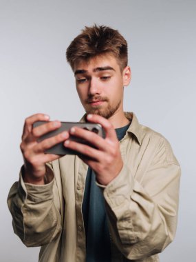 Genç adam akıllı telefon oyunlarına ve günlük kıyafetlere odaklanmış.