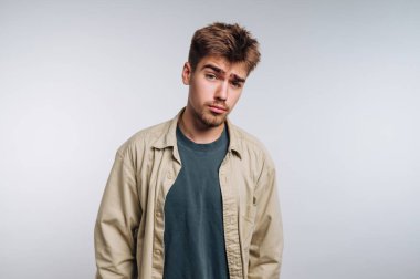 Yüzünde şüpheli bir ifade olan genç bir adam, günlük kıyafetler giyiyor..