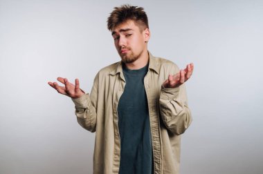 Kafası karışmış bir ifadeyle omuz silken genç bir adam, günlük kıyafetler giyiyor..