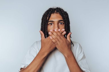 Örgülü saçlı bir insan iki eliyle ağzını kapatır ve şaşkınlığını gösterir..