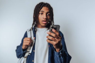 Sırt çantalı genç adam akıllı telefona şaşırmış görünüyor..