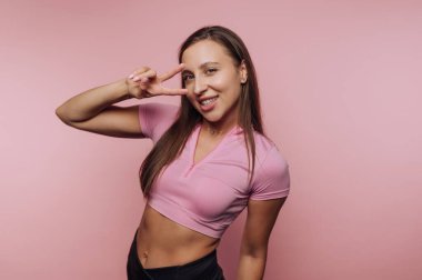 Pembe bluzlu gülümseyen kadın pembe arka planda barış işareti yapıyor..