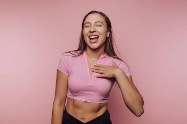 Pembe kesim bluzlu neşeli bir kadın pembe bir arka plana gülüyor..