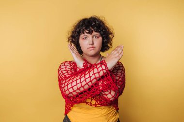A fashion model stands confidently, expressing style and individuality while wearing a striking red netted top over a yellow base. The bright yellow background enhances the vibrant look.