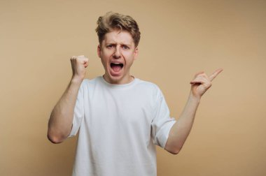 A young man is expressing intense emotion, raising his fists and shouting with joy. His background is a simple light brown, highlighting his energetic expression and enthusiasm.