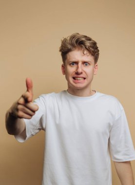 A young man with blonde hair shows an angry expression while pointing his finger. The plain background highlights his emotions clearly.