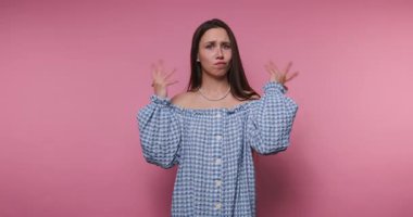 footage of young woman expresses confusion while dressed in a blue gingham outfit on pink background