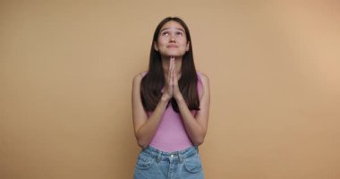 footage of young woman raising her hands in prayer conveys hope and aspiration, representing deep emotions on beige background