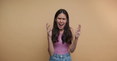 footage of young woman exhibits visible frustration and distress with an expressive hand gesture and a tense facial expression on beige background