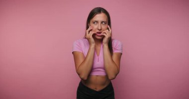 footage of young playful woman showcases a funny face, highlighting the light-hearted nature on pink background