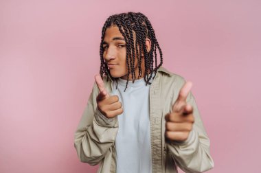 A young individual with braided hair strikes a playful pose, pointing fingers in a fun way. The bright pink background adds to the lively atmosphere of this scene.