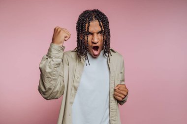 A young person with braided hair celebrates with a raised fist and wide mouth in a fun and carefree way. The bright pink background adds to the lively atmosphere.