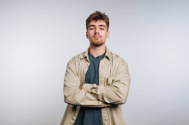 A young man stands confidently with his arms crossed, wearing a light-colored shirt over a dark t-shirt. He displays a calm expression, adding a relaxed yet assertive vibe.