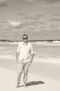 Bir adam sahilde duruyor ve ellerini cebine sokuyor.