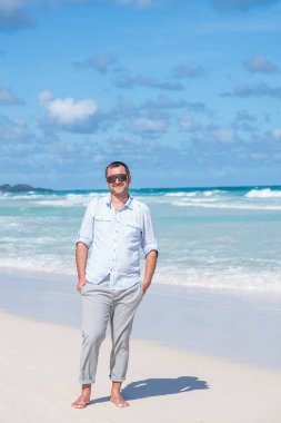 Bir adam sahilde duruyor ve ellerini cebine sokuyor.