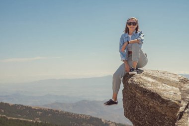 Güzel kız dağlarda büyük bir taşın üzerinde oturuyor.