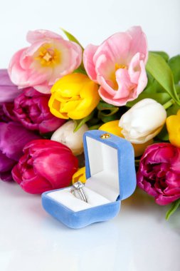 White gold ring as a gift for a woman for a holiday. Congratulations on Valentine's Day, birthday, engagement, wedding. Bouquet of tulips and box with ring on white background