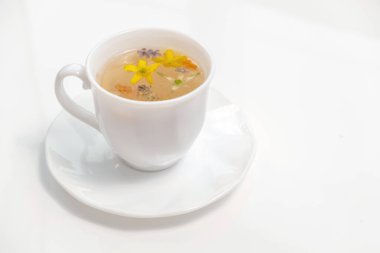 Rahatlamak ve iyileşmek için şifalı bitkiler ve çiçeklerle dolu beyaz bir fincanda sağlıklı bitki çayı.