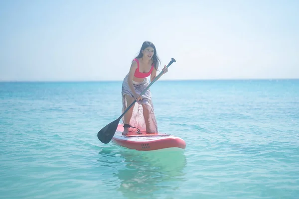 An Asian woman, a tourist, paddling a boat, canoe, kayak or surfboard with clear blue turquoise seawater, Andaman sea in Phuket island in summer season, Thailand. Water in ocean