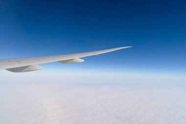 Seyahat ve ulaşım kavramında pencereden mavi gökyüzü ile bulutların üzerinde uçan bir uçak jeti kanadı. Doğa manzarası arka planı.