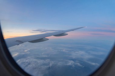 Seyahat ve ulaşım kavramında pencereden mavi gökyüzü ile bulutların üzerinde uçan bir uçak jeti kanadı. Doğa manzarası arka planı.