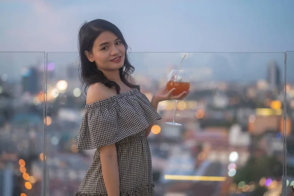一个亚洲女人的画像 晚上在有城市天际线背景的阳台天空酒吧的餐厅里 手里拿着一杯鸡尾酒啤酒 人的生活方式 — 图库照片