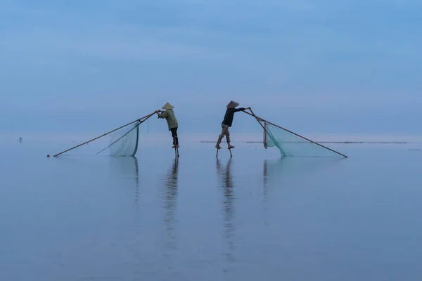 stock image Silhouette of Vietnamese fisherman holding a net for catching freshwater fish in nature lake or river with reflection in morning time in Asia in Vietnam. People.