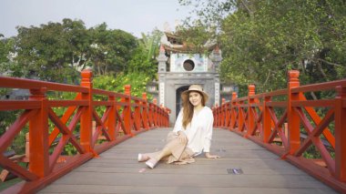 Asyalı Vietnamlı bir kadının portresi Hanoi şehir merkezindeki Hoan Kiem Gölü 'ndeki ağaçlarla halka açık park bahçesindeki Kızıl Köprü' de seyahat ediyor. Şehir, Vietnam...