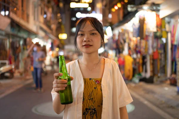 Drunk alcoholic woman Asian Vietnamese woman travel at night, drinking beer in market. People walking street fair in Hanoi city, Vietnam. Retail shops