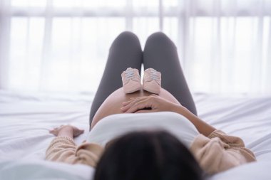 Mutlu Asyalı hamile bir kadının portresi. Yatak odasında bebek ayakkabıları var. Bebek sahibi olmak. Aile hayatı işte. Aşk.