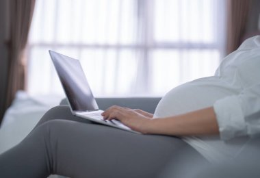 Mutlu Asyalı hamile bir kadının portresi. Evde yatak odasında ekranı olan bilgisayar dizüstü bilgisayarlı tablet cihazıyla çalışıyor. Bebek sahibi olmak. Aile hayatı işte. Annen seni seviyor.