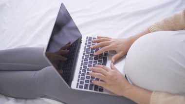 Mutlu Asyalı hamile bir kadının portresi. Evde yatak odasında ekranı olan bilgisayar dizüstü bilgisayarlı tablet cihazıyla çalışıyor. Bebek sahibi olmak. Aile hayatı işte. Annen seni seviyor.