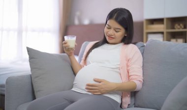 Evdeki yatak odasında kalsiyum için süt içen mutlu Asyalı hamile bir kadının portresi. Bebek sahibi olmak. Aile hayatı işte. Annen seni seviyor.