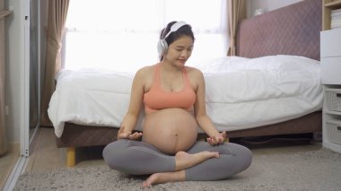 Evdeki yatak odasında mutlu bir Asyalı hamile kadının portresi. Bebek sahibi olmak. Antrenman egzersizi. Spor malzemeleriyle içeride egzersiz yap. Atletik. Aile hayatı işte. Anne sevgisi. Rekreasyon.