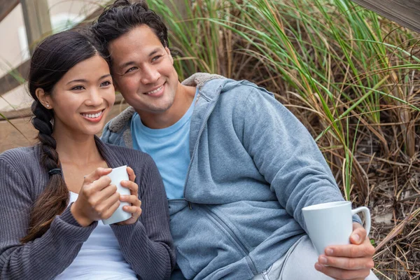 年轻的亚洲男人和女人 男孩和女孩 约会对象坐在木制台阶上俯瞰海滩 喝着茶杯或咖啡 — 图库照片