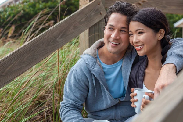 年轻的亚裔男子和女子 男孩和女孩 约会对象坐在木制台阶上俯瞰海滩 喝着茶或咖啡 — 图库照片