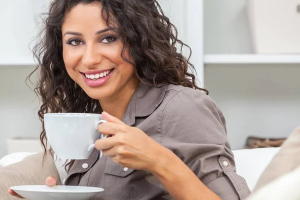 Beautiful young Latina Hispanic woman smiling, relaxing and drinking a cup of coffee or tea at home