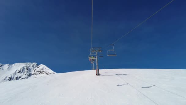 4K视频剪辑 四个人在蓝天滑雪板上坐着电梯爬山 滑雪者在下面的人行道上 — 图库视频影像