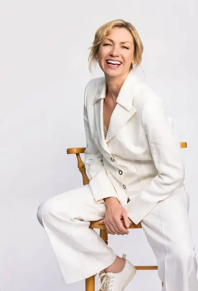 迷人而自信的微笑着聪明的中年女性画像坐在长椅上 身穿白色西服 图库图片