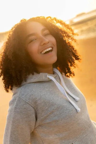 屋外のポートレートの美しい幸せな混合民族のアフリカ系アメリカ人女の子黄金の夕日太陽の下で完璧な歯で笑って笑ってビーチで 代女性若い女性 ストック写真