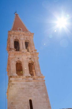 Sun in a blue sky behind the tower of The Church of St Stephen, Stari Grad, Hvar Island, Croatia clipart