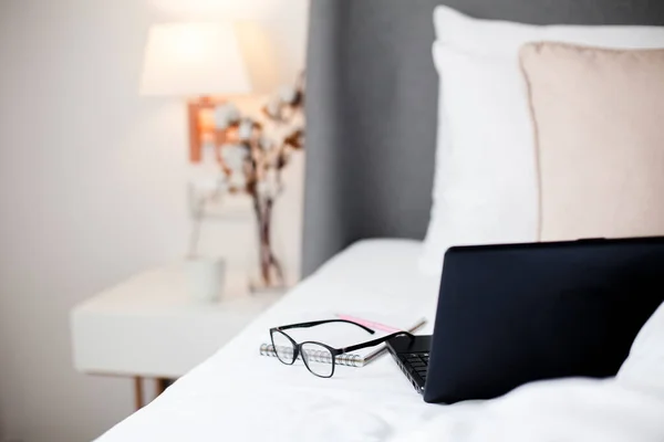 Laptop, glasses in bed. Remote working from home office. Freelance workplace in cozy bedroom. Distance learning, online education, wellbeing, healthcare.
