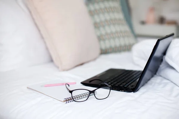 Laptop and glasses on bed. Remote working from home office. Freelance workplace in bedroom. Distance learning, online education, healthcare online.
